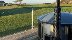 A portable wood stove on a deck with a view of a grassy field and a body of water in the background. - Beautiful holiday home on Nordals, Vinkelbæk 40 (Nordborg)