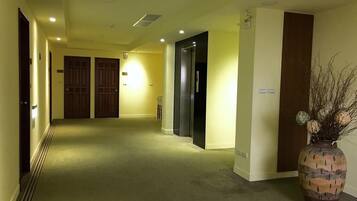A hotel hallway with carpeted floors, wooden doors, and a large vase with dried branches.