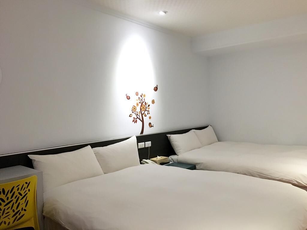 A hotel room with two beds, a nightstand, a lamp, and a wall decoration.