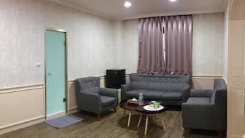 A living room with a teal door, a grey sofa, two armchairs, a small coffee table, and a speaker.