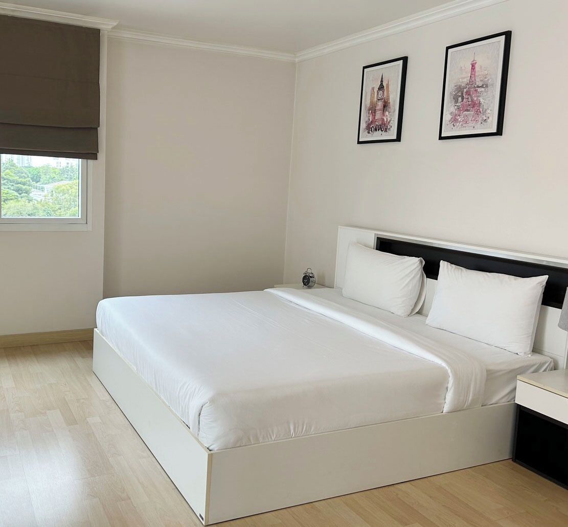 A bedroom with a large bed, a nightstand, a window with a blind, and two framed pictures on the wall.