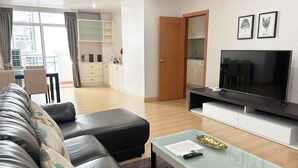 A modern living room with a leather sofa, a glass coffee table, a flat-screen TV, and a kitchen area in the background. - Pacific Residence 39 (Bangkok)
