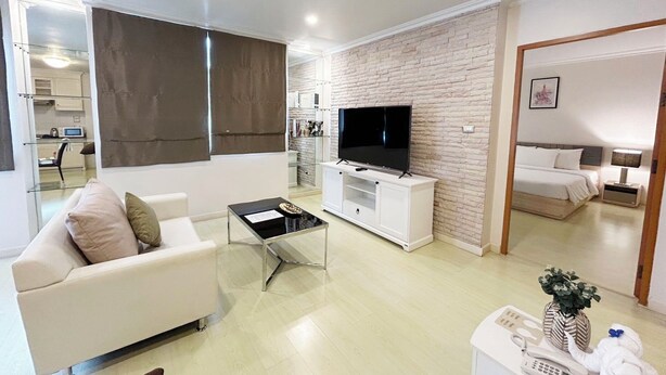 A modern living room with a flat-screen TV, a sofa, a coffee table, and a kitchen area in the background. - Pacific Residence 39 (Bangkok)