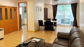 A spacious living room with a leather sofa, a dining table with chairs, and a kitchen visible through an open door. - Pacific Residence 39 (Bangkok)