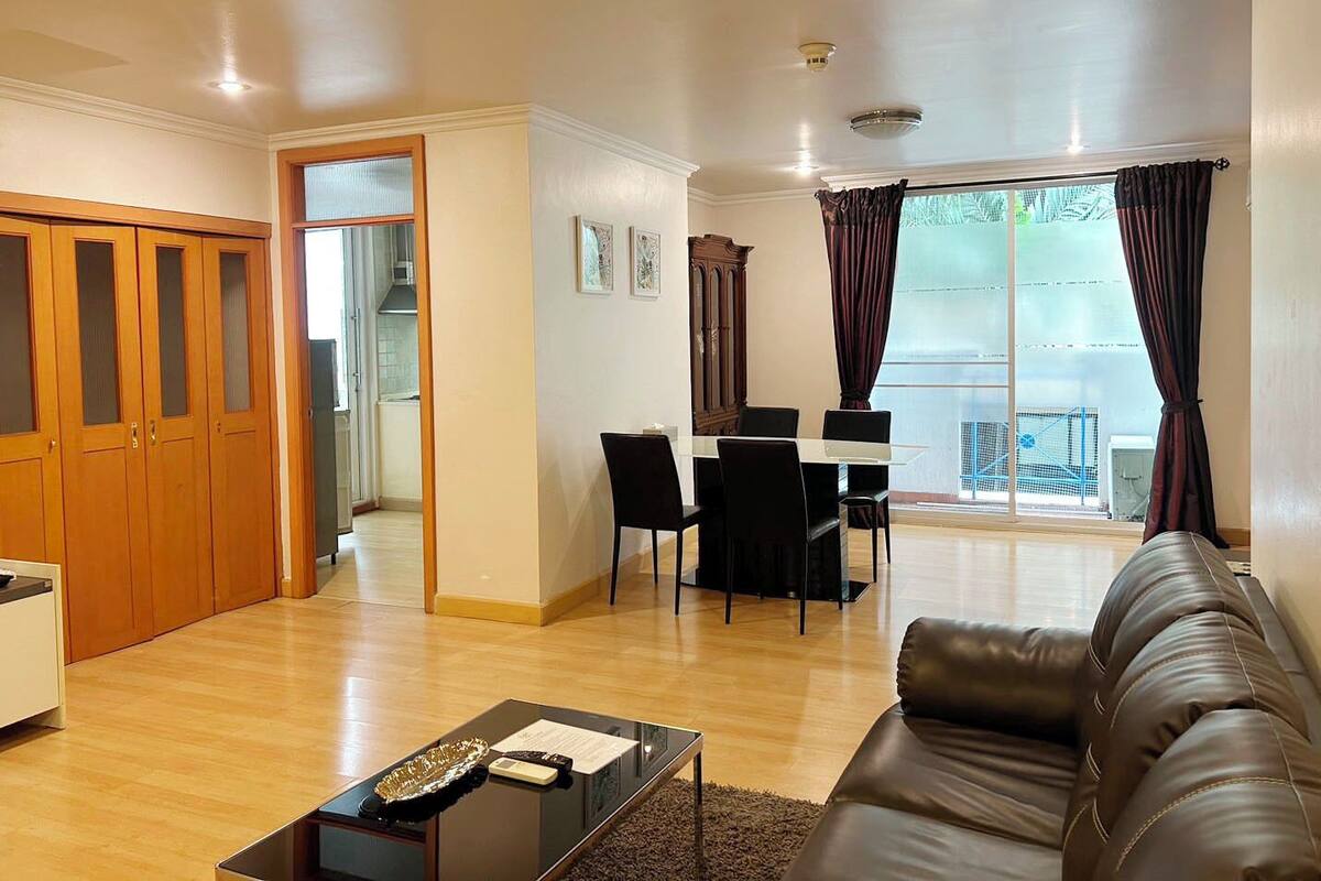 Un salón amplio con un sofá de cuero, una mesa de comedor con sillas y una cocina visible a través de una puerta abierta.