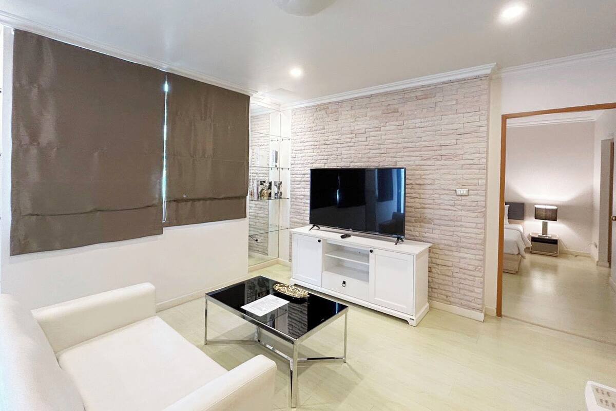 Una sala de estar moderna con un televisor de pantalla plana, muebles blancos y una pared con diseño de ladrillo.