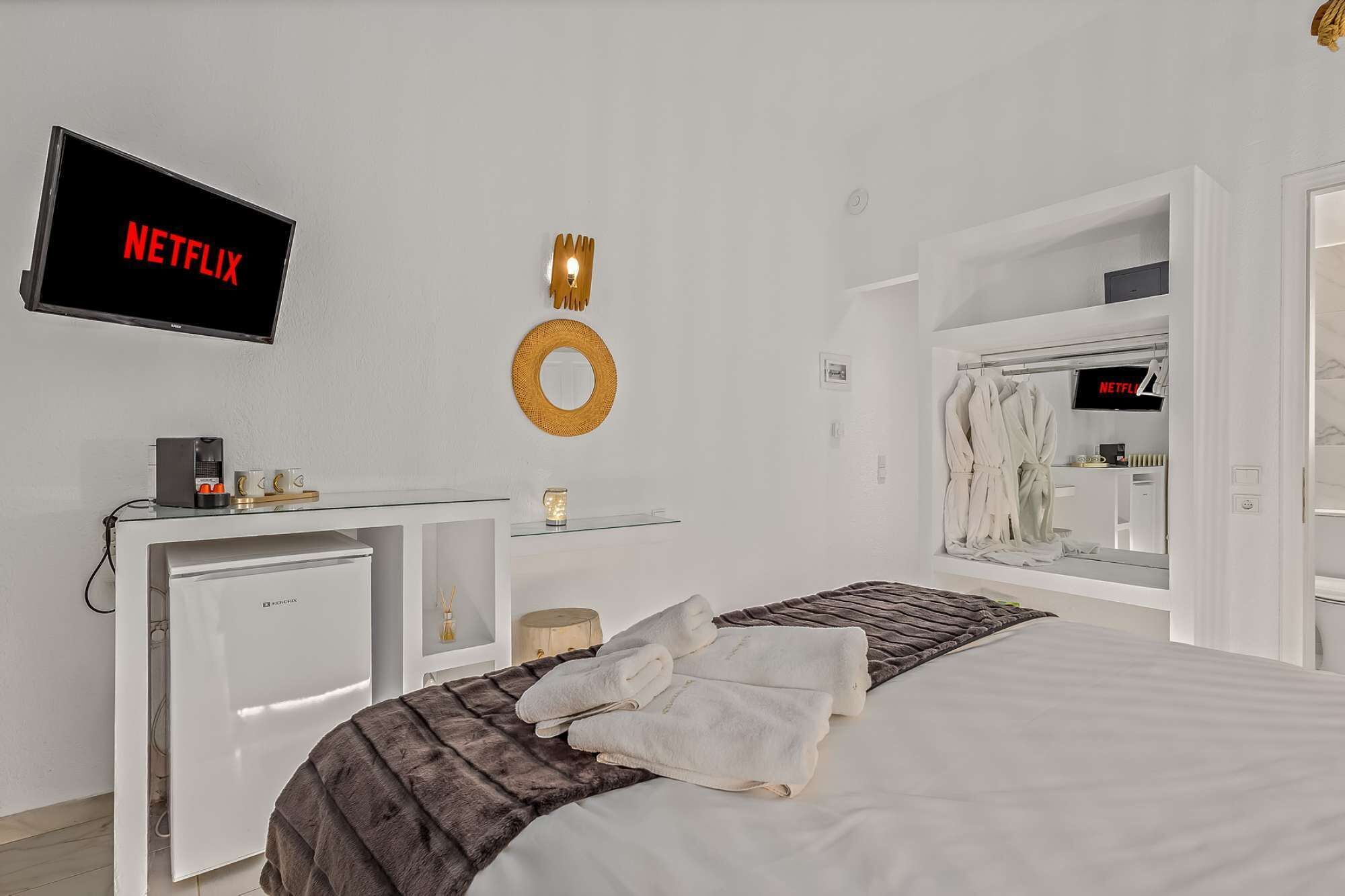 A bedroom with a bed, a desk, a mirror, a TV, and a wardrobe.