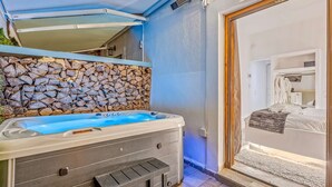 A spa area with a hot tub, stone wall, and a view into a bedroom with a bed and robe. - Blue Mountain Guesthouse "Estrella” (Arachova)