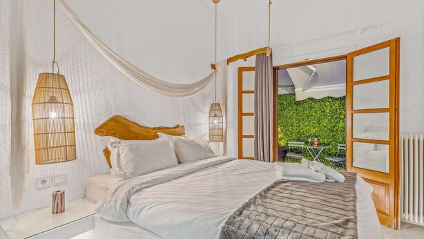 A bedroom with a large bed, a glass bedside table, a hanging light fixture, and a view of a green garden through open windows. - Blue Mountain Guesthouse "Estrella” (Arachova)