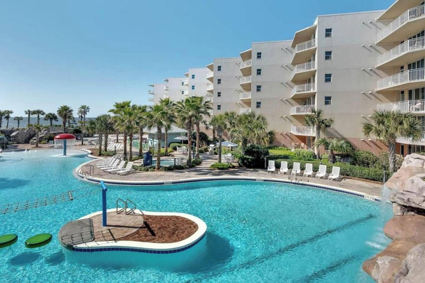 A hotel with a swimming pool, palm trees, and a view of the ocean.