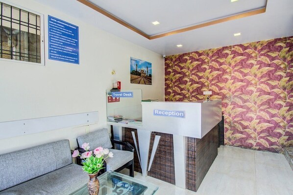 A hotel reception area with a reception desk, a travel desk, and a seating area with a sofa and a table with a vase of flowers.