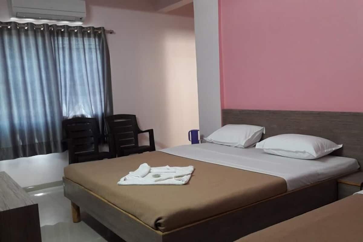 Quarto de hotel com cama, uma cadeira, escrivaninha e janela com cortinas.