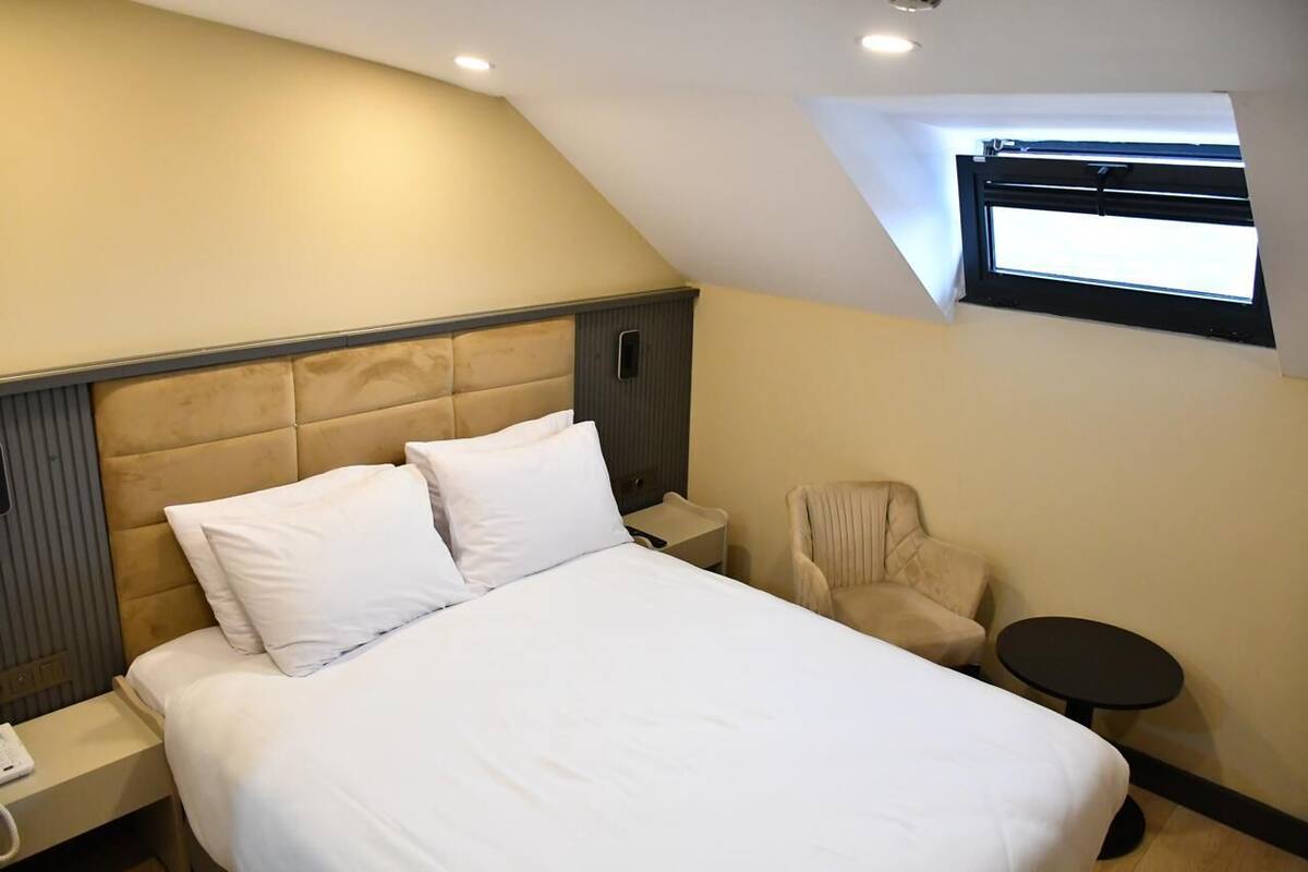 A hotel room with a large bed, a chair, a small table, a nightstand, and a window with a view.