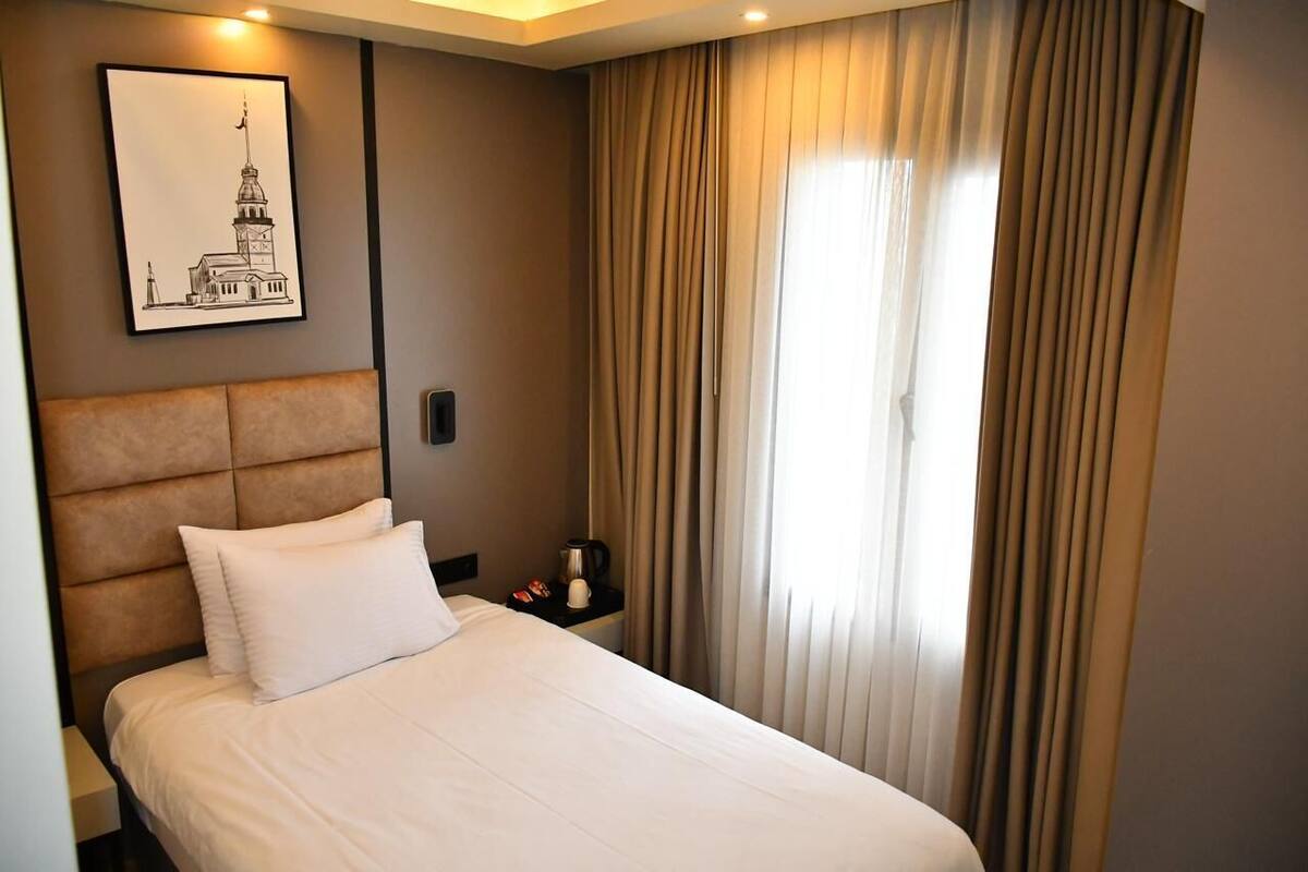 A hotel room with a bed, a nightstand, a framed picture on the wall, and a window with curtains.