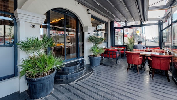 An outdoor seating area with potted plants, red chairs, and a glass enclosure. - Frt Airlines Hotel - Istanbul Airport (Arnavutköy)