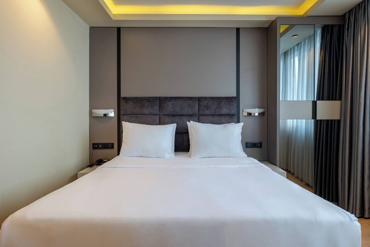 A modern hotel room with a large bed, two bedside tables, and a headboard with integrated lighting.