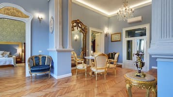 A luxurious room with a herringbone wooden floor, ornate gold-framed furniture, and a chandelier.