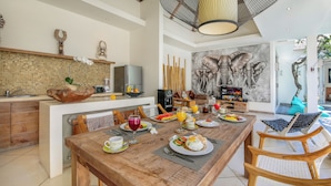 Un vaste espace de salle à manger avec une table en bois dressée pour le petit-déjeuner, une cuisine au design moderne et une grande fresque représentant un éléphant sur le mur.