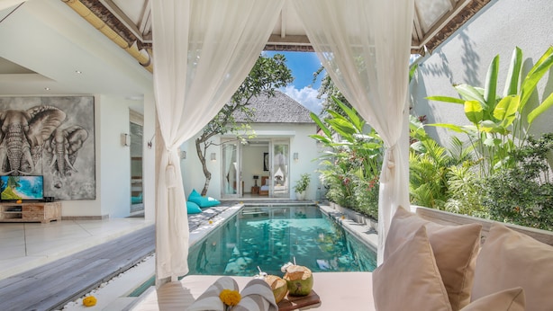 Un espace aménagé au bord de la piscine, avec un lit, un tableau représentant des éléphants et une vue sur une maison.