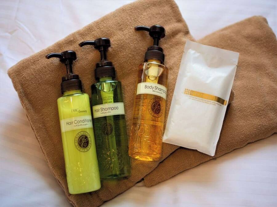 A set of toiletries on a brown towel, including hair conditioner, hair shampoo, body shampoo, and a white packet.