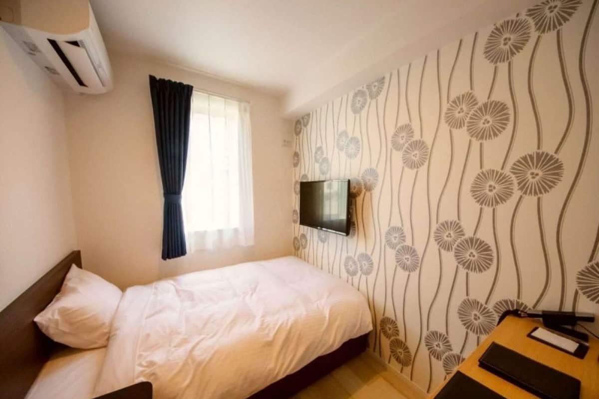 A bedroom with a bed, a TV mounted on the wall, and a patterned wallpaper.