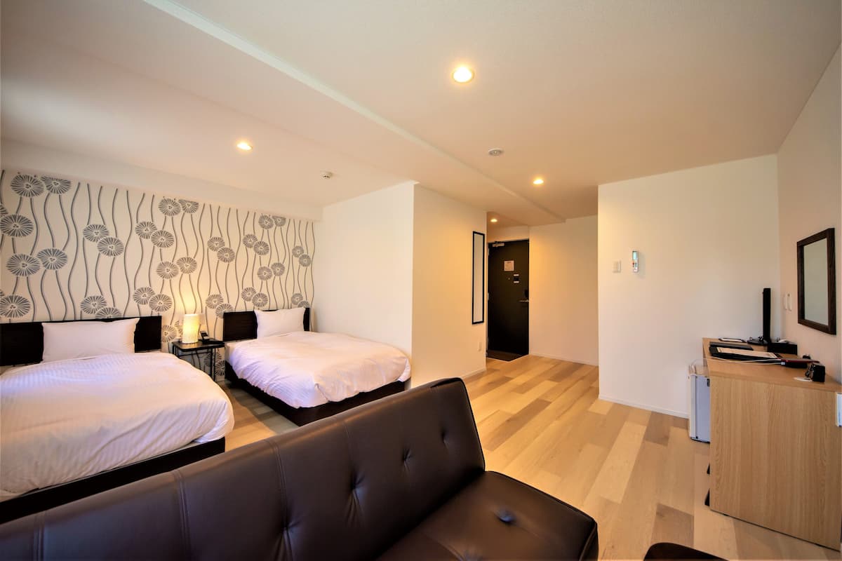 A hotel room with two beds, a sofa, a desk, and a wall with a floral pattern.
