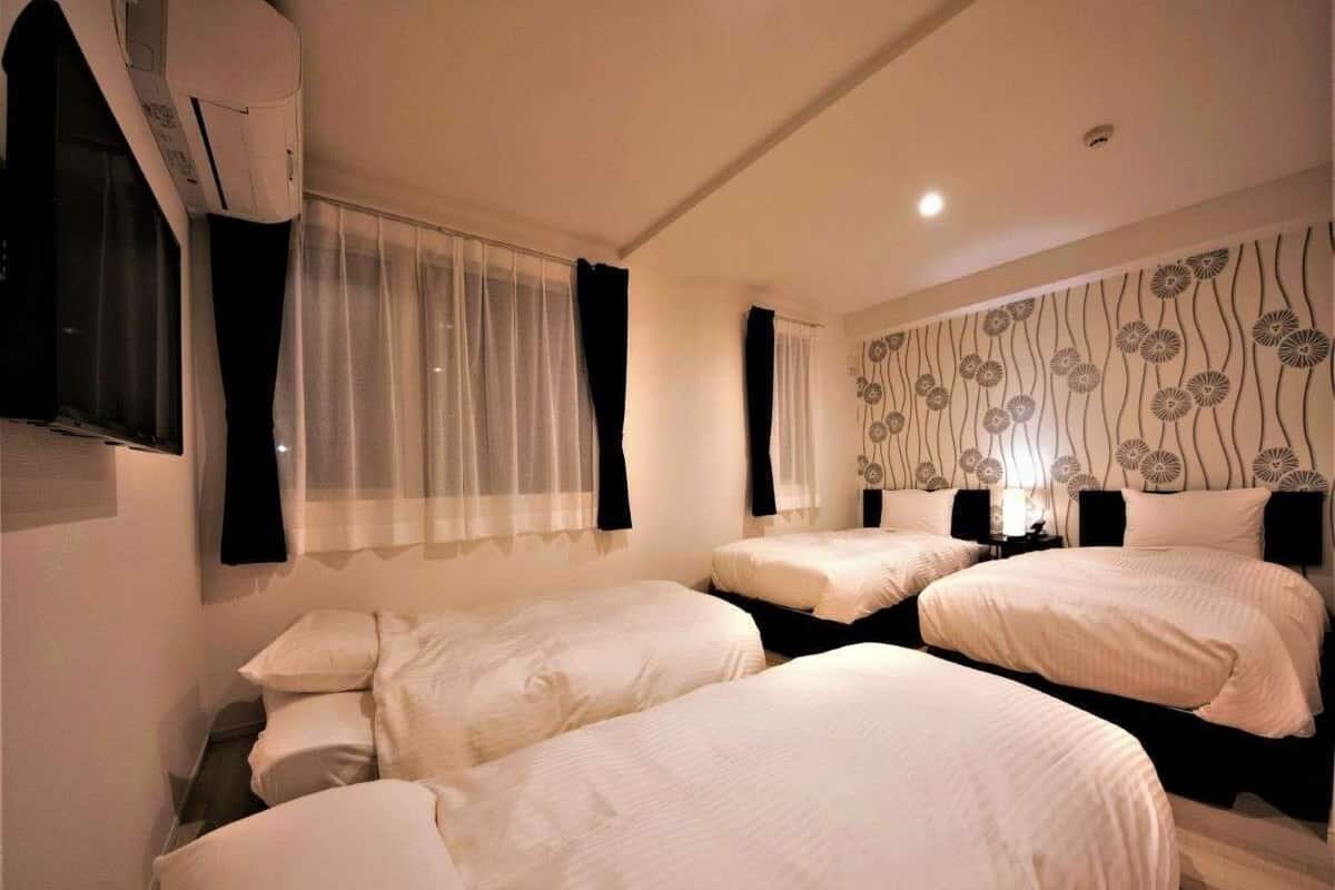 A hotel room with three single beds, a flat-screen TV mounted on the wall, and a decorative wall panel.