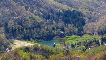 A mountainous landscape with a lake, forested areas, and a small building near the water.