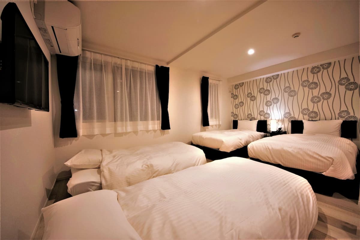 A hotel room with three beds, a TV, an air conditioning unit, and a patterned wall.