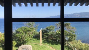 Vista a través de una ventana con techo de madera, que da a un paisaje costero con árboles y cielo despejado.