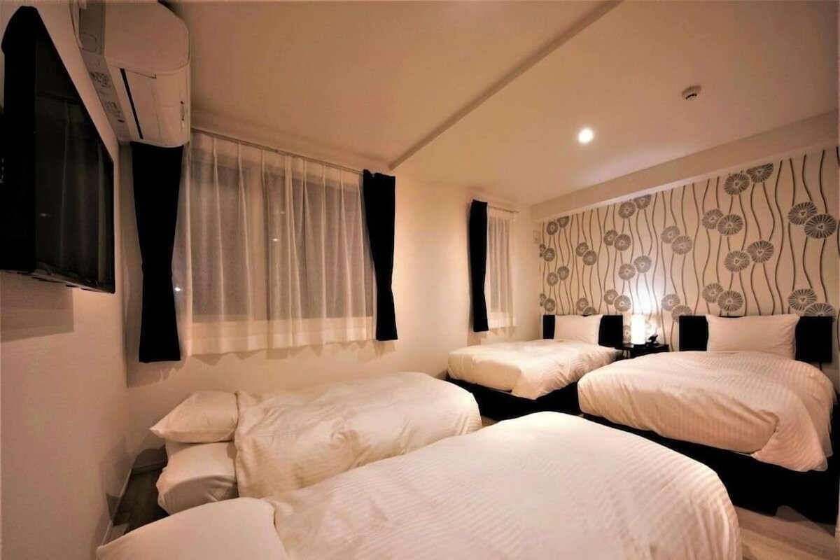A hotel room with two beds, a window with curtains, a wall with a floral pattern, and an air conditioning unit.