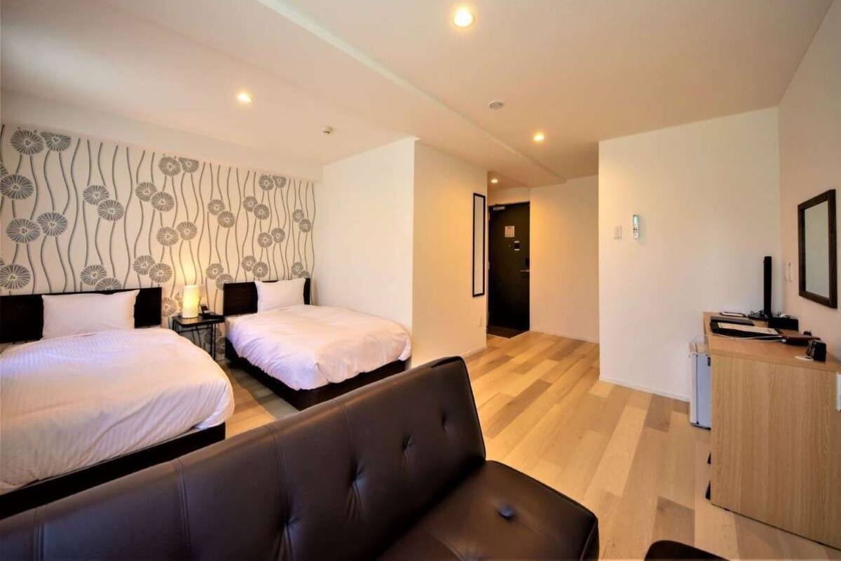 A hotel room with two beds, a sofa, a desk, and a wall with a floral pattern.