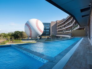 Una piscina con una gran escultura de béisbol, blanca y roja, al fondo.