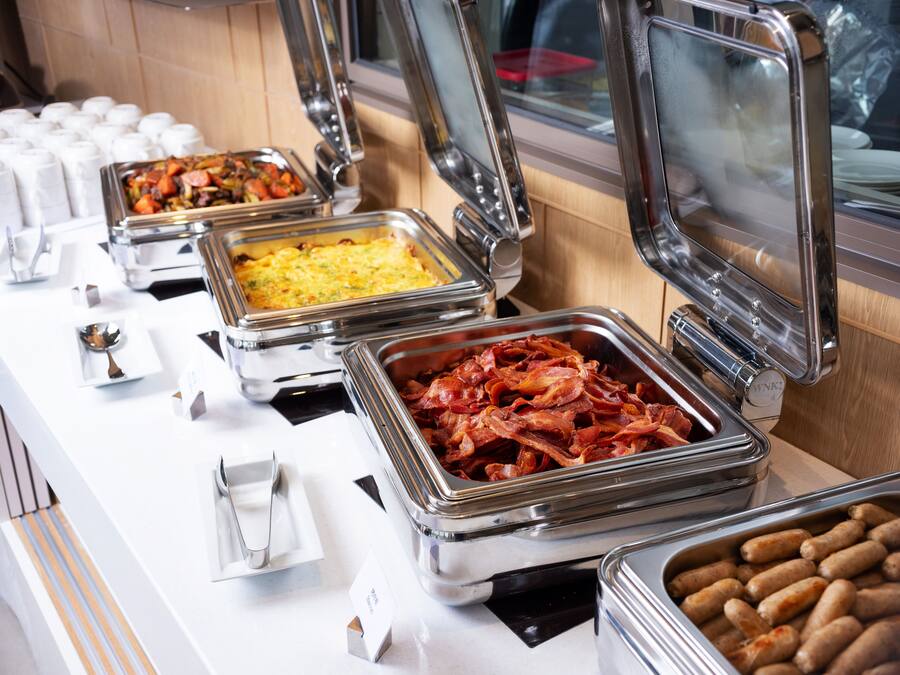 Un buffet proposant une variété de plats, notamment du bacon, des œufs et des saucisses.