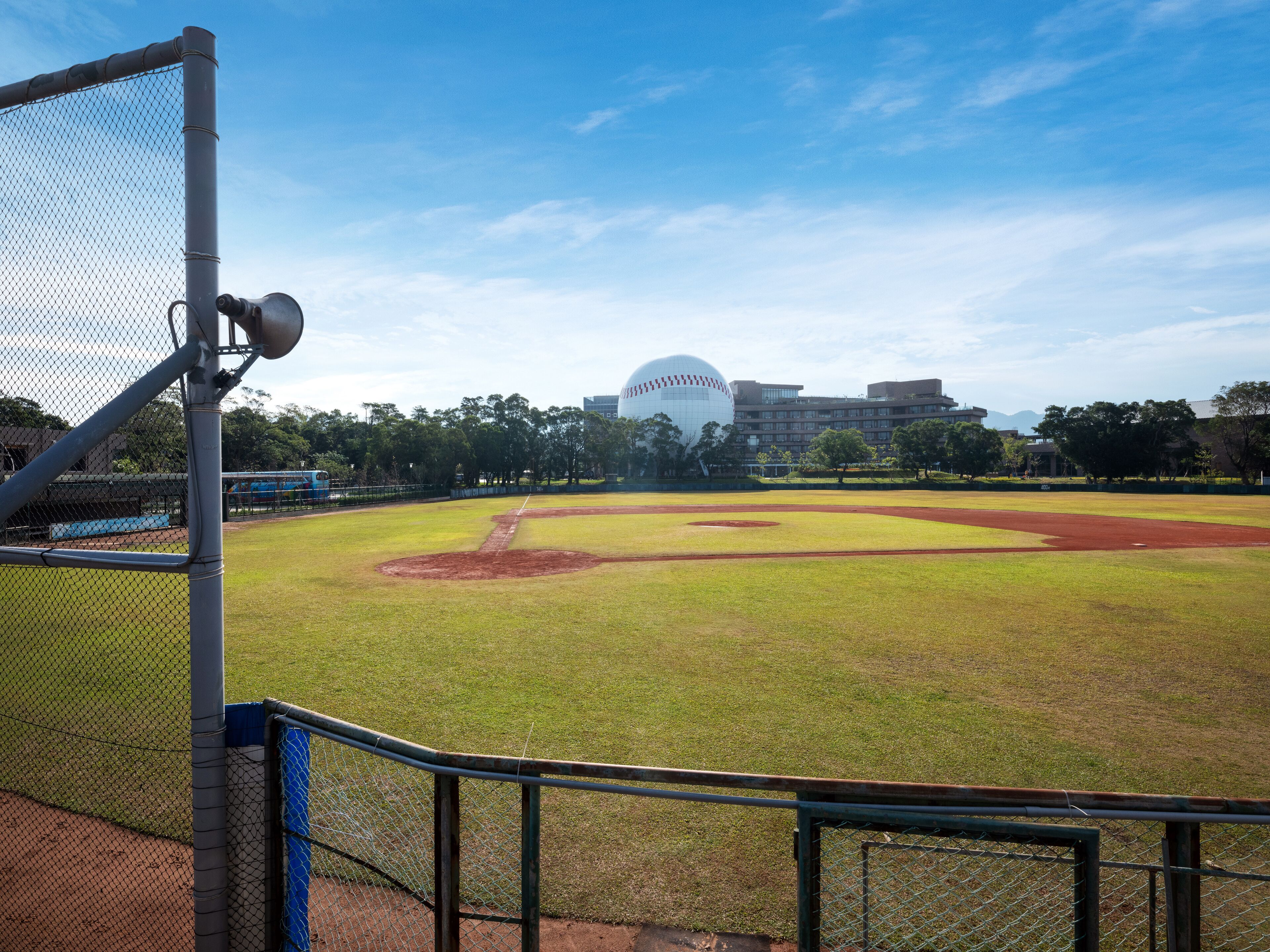 A baseball field with a chain-link fence, a dugout, and a large dome structure in the background.