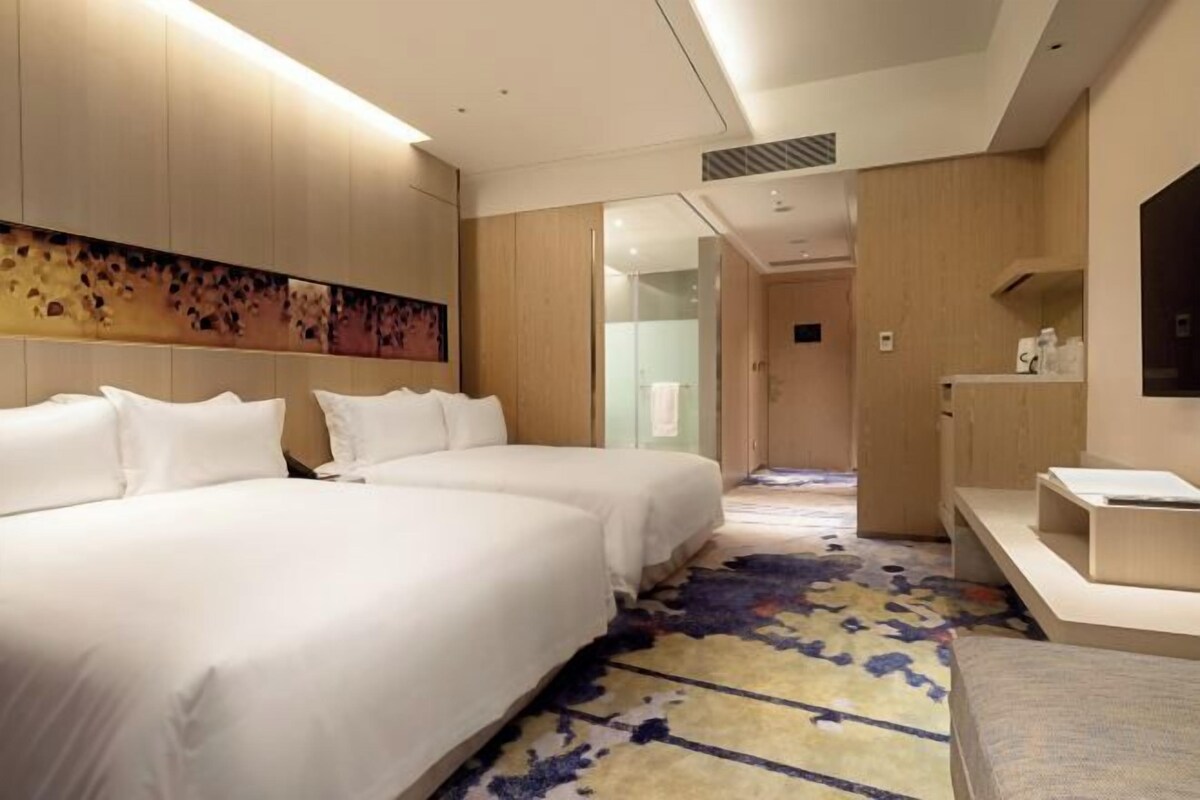 A hotel room with two beds, a desk, and a shower area.