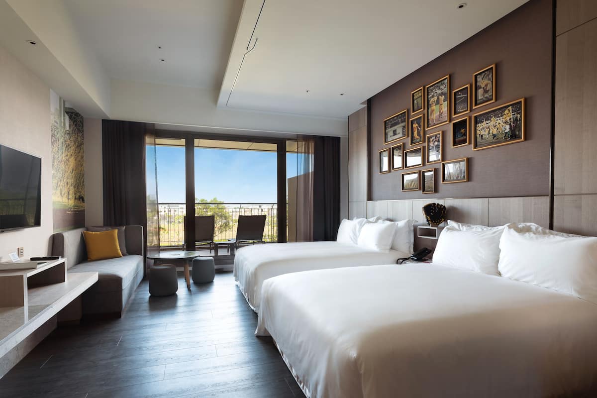 A hotel room with two large beds, a TV, a balcony with a view, and a wall decorated with framed pictures.