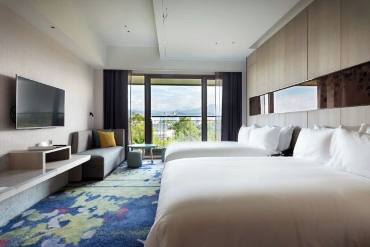 Habitación de hotel con una cama grande, televisión, zona de estar y vistas al exterior.
