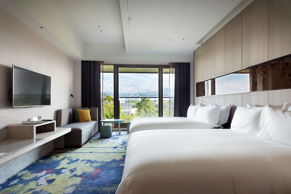 A modern hotel room with a large bed, a sofa, a TV, and a balcony with a city view.