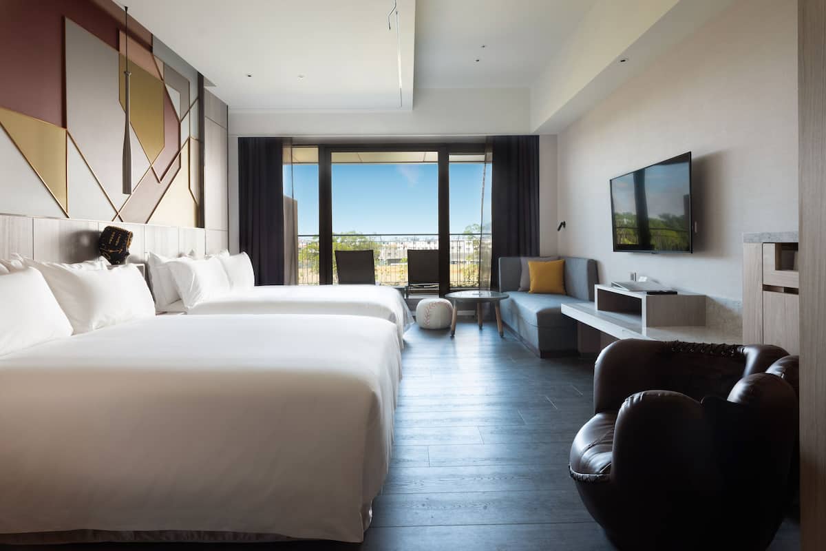 A modern hotel room with a large bed, a sofa, a TV, and a balcony with a view.