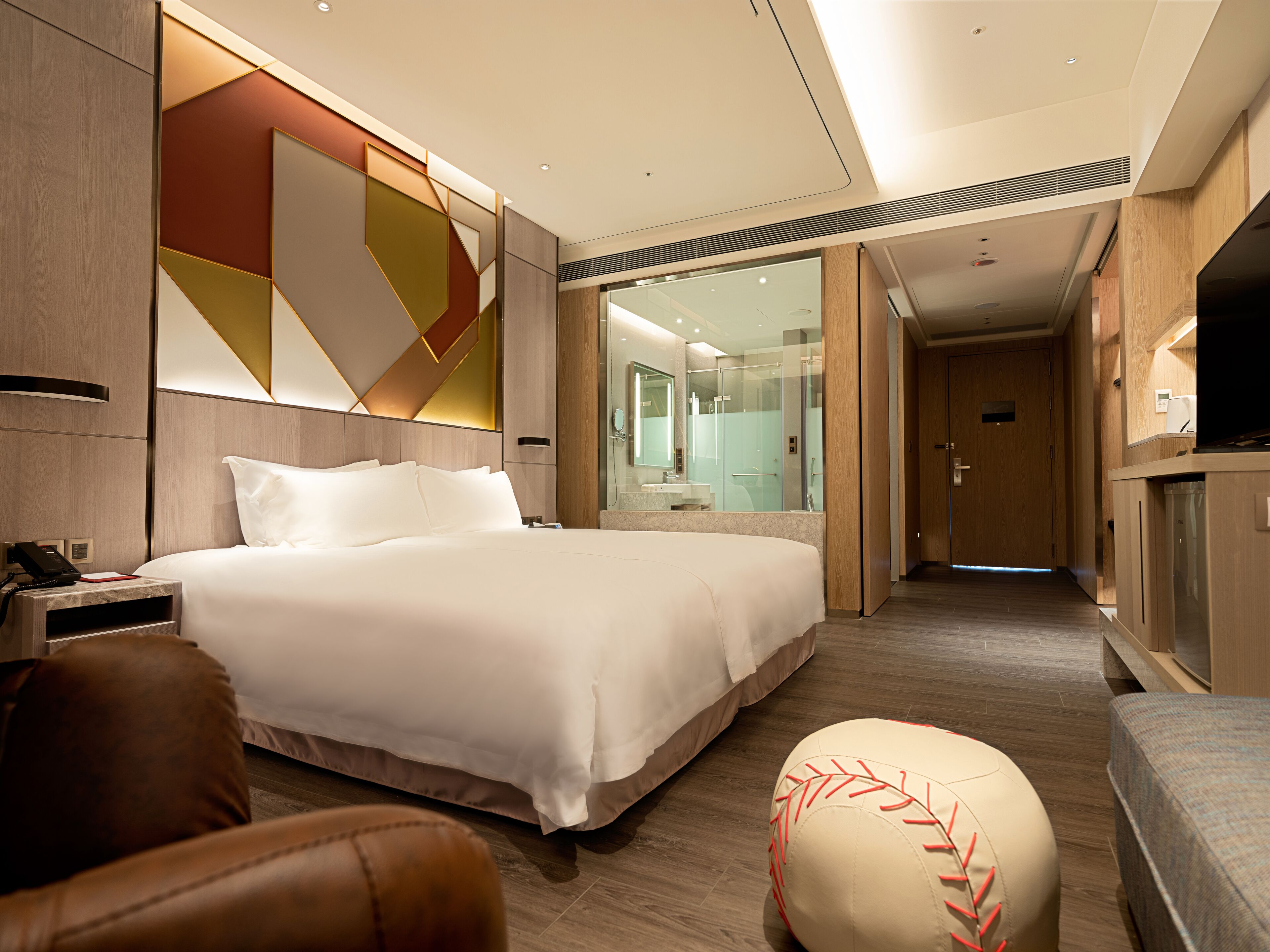 Una habitación de hotel moderna con una cama grande, un escritorio con teléfono, una televisión y un baño con cabina de ducha de vidrio.