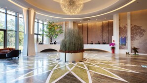 A spacious lobby with a central decorative plant, a modern chandelier, and a reception desk with staff. - Fame Hall Garden Hotel (Taoyuan City)