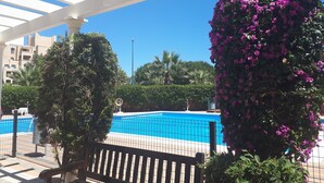 Un área de piscina con una pérgola blanca, un banco y una decoración floral colgante.