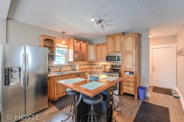 A modern kitchen with stainless steel appliances, wooden cabinets, and a central island with stools.