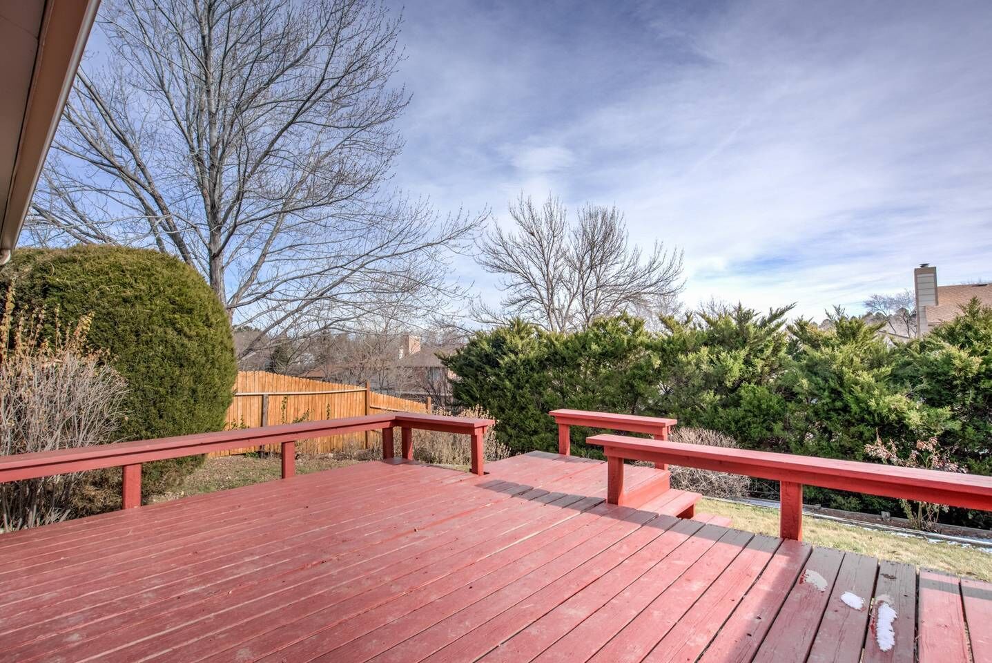 A wooden deck with red railings, surrounded by trees and a wooden fence.