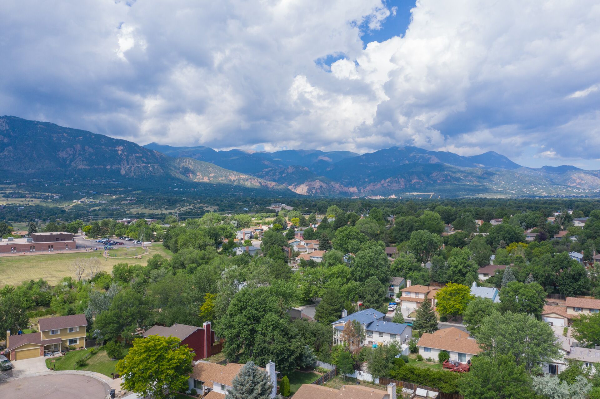 Un quartier résidentiel avec des maisons, une école et des montagnes en arrière-plan.