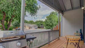 Un espace extérieur abrité, doté d’un barbecue, d’une terrasse en bois et offrant une vue sur une rue résidentielle.