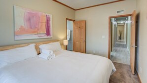 Une chambre d’hôtel avec un grand lit, un ventilateur de plafond, une porte en bois et un couloir menant à une autre chambre.
