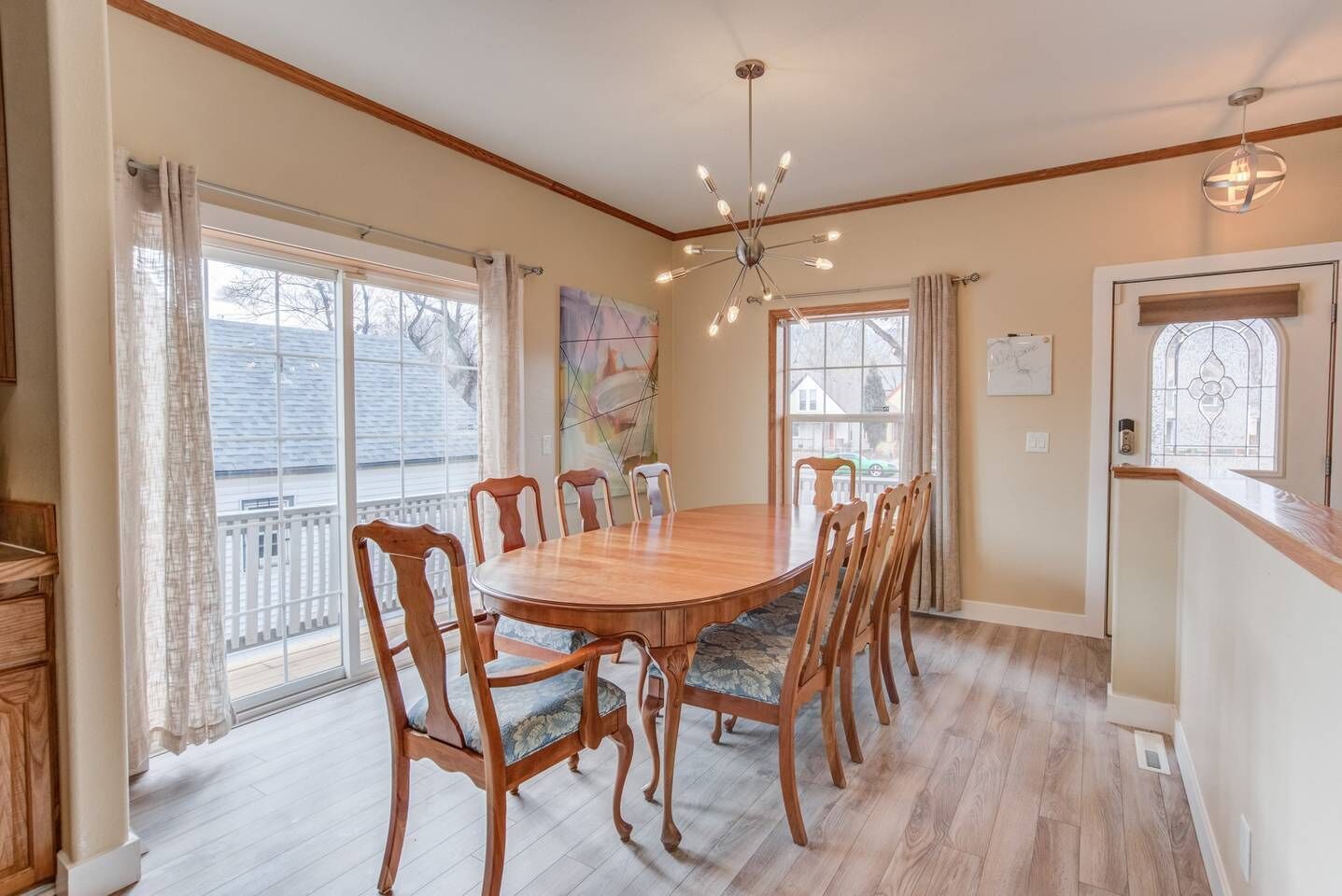 A dining room with a wooden table and chairs, large windows, and a chandelier.
