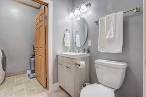 A bathroom with a toilet, sink, and mirror. There is a towel rack and a shower area visible.